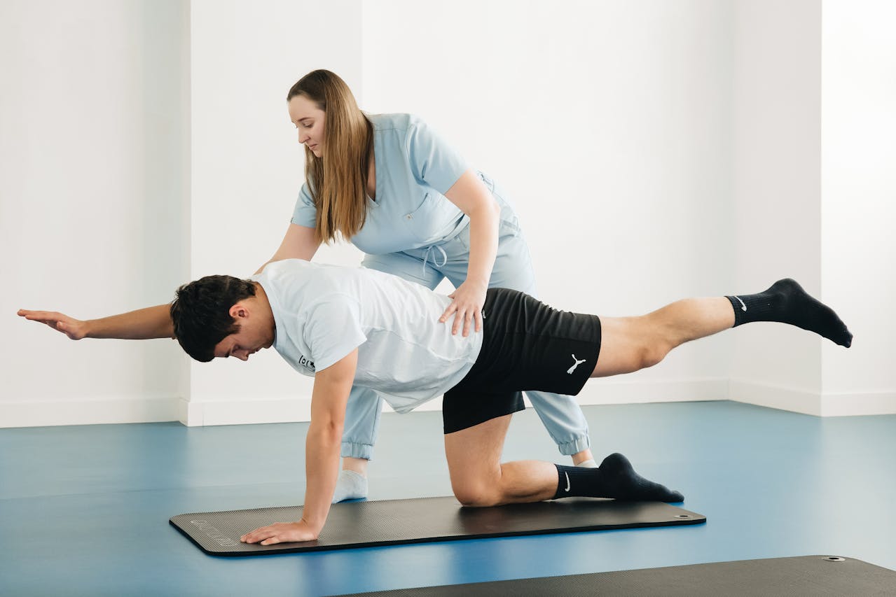 A woman supports a man by holding her hand during a yoga class, emphasizing physiotherapy-focused balance training